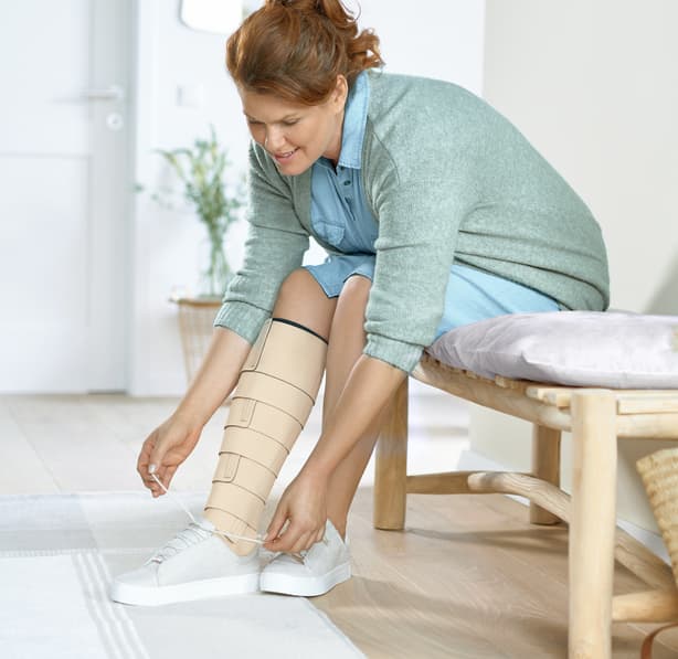 Eine Frau zieht sich die schuhe an und tragt an einem Bein einen Kompressionsverband. Eine Frau zieht sich die schuhe an und tragt an einem Bein einen Kompressionsverband.